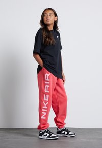 Camiseta negra de manga corta con el logo de Nike. Pantalones de chándal rosas con "NIKE AIR" impreso en blanco. Zapatillas negras con acentos blancos. Ropa casual básica.