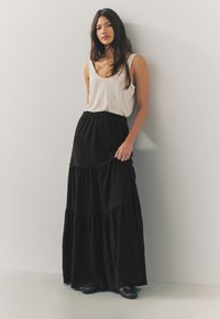 Czarna, warstwowa maxi spódnica wykonana z lekkiego materiału, zestawiona z białym prążkowanym topem na ramiączkach. Stylizację uzupełniają czarne, płaskie sandały.