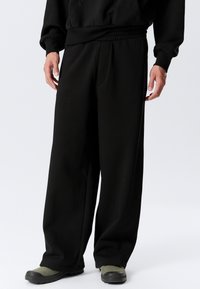 Black sweatpants with a relaxed fit, elastic waistband, and side pockets. Material appears soft, with a smooth texture and minimal detailing.