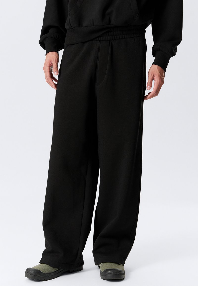 Black sweatpants with a relaxed fit, elastic waistband, and side pockets. Material appears soft, with a smooth texture and minimal detailing.