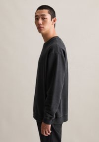 Donkergrijze katoenen sweatshirt met een ronde hals, lange mouwen en geribbelde manchetten. Strakke textuur en relaxte pasvorm, weergegeven op een model.