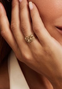 Gold-Multibandring mit ineinandergreifenden Ringen, die glatte und strukturierte Abschnitte aufweisen, getragen an einer Hand mit sorgfältig manikürten Nägeln.