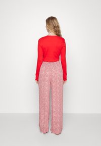 Top de manga longa com riscas vermelhas, combinado com umas calças largas de cintura alta em padrão floral rosa claro. Tecido suave, ajuste descontraído.
