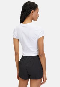 Vit kortärmad crop top kombinerad med svarta shorts med elastiskt midjeband, som visar en enkel design och en jämn textur, sedd bakifrån.