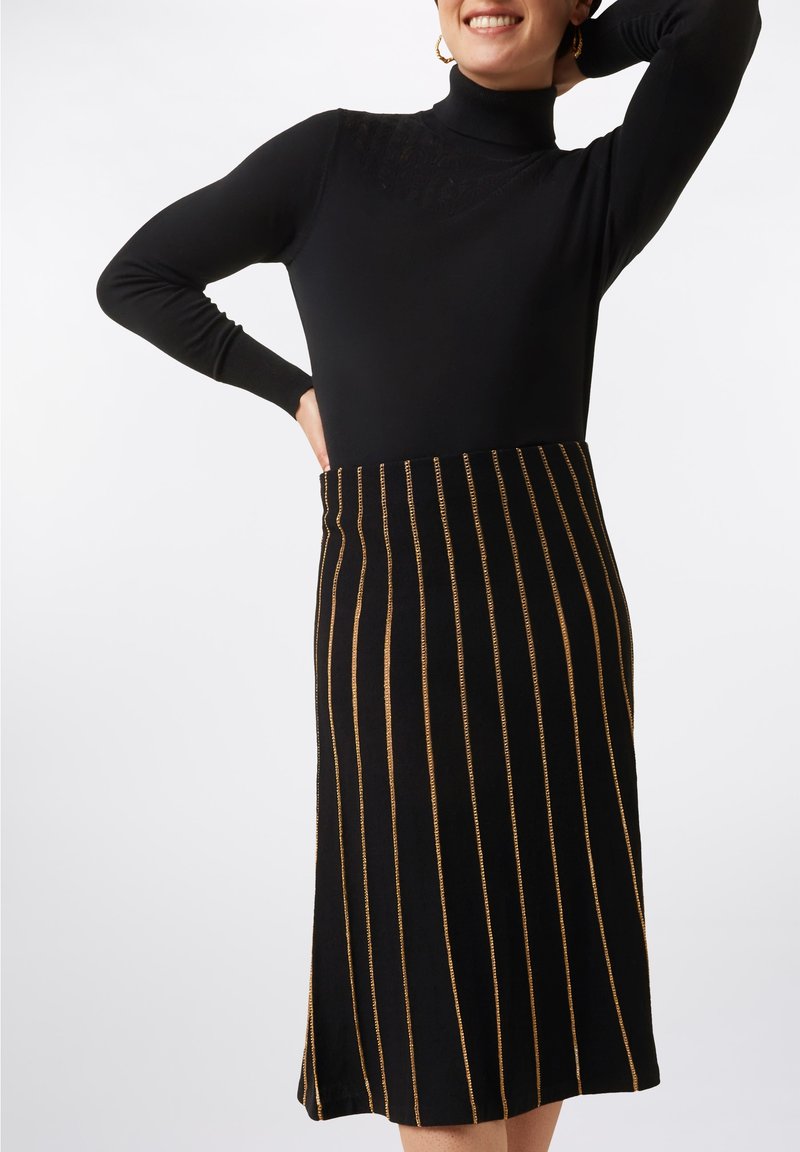 Black knit turtleneck top paired with a mid-length black skirt featuring gold vertical stripes and a straight hem. Smooth texture.