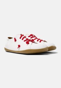Scarpe da ginnastica bianche con lacci rossi, punta arrotondata e suola in gomma marrone. Presentano nodi decorativi sulla tomaia per un tocco in più.
