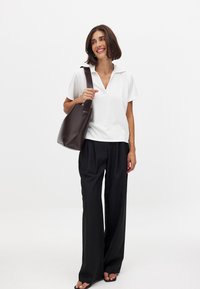 Balts īsās piedurknes polo krekls ar V veida kakla izgriezumu, kas kombinēts ar brīvām melnām biksēm. Uz kreisās rokas nēsā brūnu ādas pleca somu.