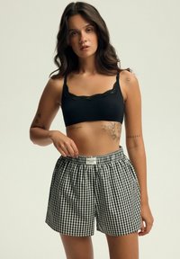 Czarny biustonosz z koronkowym wykończeniem połączony z luźnymi czarno-białymi szortami w kratę gingham. Posiada elastyczny pas i casualowy styl.