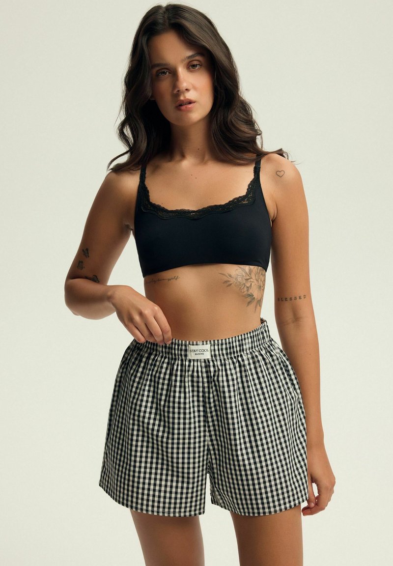 Czarny biustonosz z koronkowym wykończeniem połączony z luźnymi czarno-białymi szortami w kratę gingham. Posiada elastyczny pas i casualowy styl.
