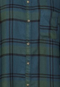 Koszula w kratę w odcieniach niebieskiego i zielonego, z czarnymi paskami, z guzikami z przodu i kieszenią na piersi. Miękka tekstura materiału.