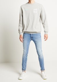 Grå sweatshirt med text i vitt och ljusblått, parat med ljusblå jeans och vita sneakers. Enkelt mönster, avslappnad passform.
