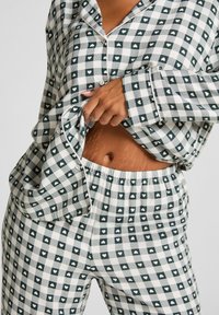 Zielono-biały pidżama w kratkę z wzorem serc. Koszula z guzikami i elastyczny pas w spodniach. Miękka tkanina; luźny krój.