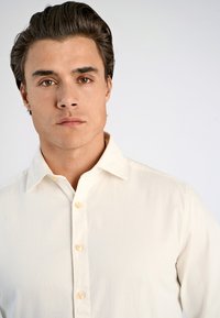 Camicia beige a maniche lunghe in cotone, con patta abbottonata e colletto a punta, dal tessuto morbido e dalla vestibilità classica.