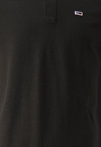 Czarny polo wykonany z bawełny, z klasycznym kołnierzykiem i małym logo w kolorze białym, czerwonym i niebieskim na lewej stronie klatki piersiowej.