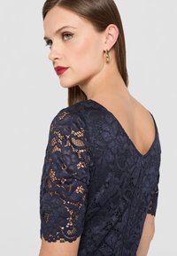 Abito in pizzo navy con motivi floreali, maniche corte e scollatura a V sul retro, completato da una zip nascosta sulla parte posteriore.