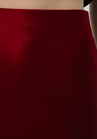 Czerwona dopasowana spódnica z gładkiego, teksturowanego materiału. Posiada wysoki pas i subtelne przeszycia po bokach. Bez widocznych elementów metalowych.