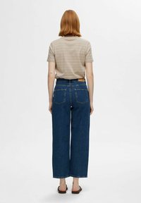 Camiseta a rayas beige combinada con unos pantalones vaqueros de mezclilla azul de pierna ancha y cintura alta. Los pantalones tienen dos bolsillos traseros y una etiqueta de cuero marrón en la cintura.