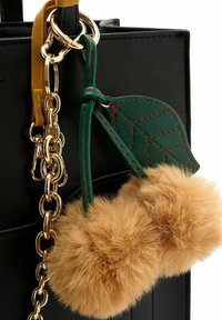 Borsa nera con catena dorata, caratterizzata da due pompon marroni pelosi e un accento in pelle verde con cuciture rosse.