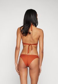 Rūsganā krāsā bikini ar halter topu, kuram ir regulējamas saites un atpakaļējo saišu detaļa, apvienots ar saderīgu zemu vidukļa apakšdaļu. Gluda tekstūra.
