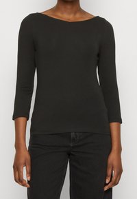 Svart, figurnära långärmad topp med båtformad halsringning. Tillverkad av ett slätt material, har trekvartsärmar och en enkel, ren design.