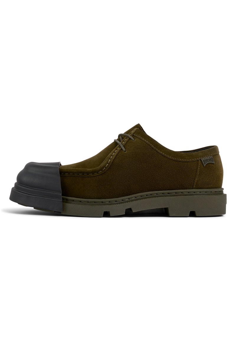 Scarpe scamosciate verde oliva con punta in gomma nera, caratterizzate da un design con lacci e una suola con texture. Dettagli cuciti lungo i bordi.