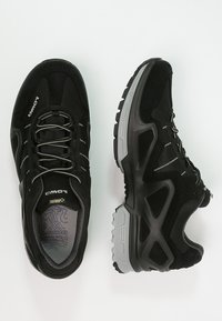 Schwarze Sportschuhe mit einem Obermaterial aus strukturiertem Stoff, grauen Akzenten, verstärkter Zehenkappe und einer gepolsterten Sohle mit einem profilierten Muster.