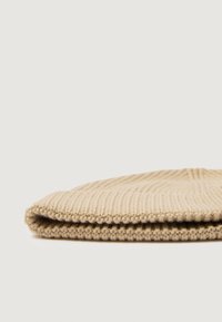 Kootud beež beanie ribakat tekstuuri, millel on volditud äär ja pehme, siledalt lõng. Nurgeline vaade, mis esitleb selle kuju ja disainijooni.