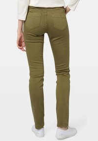 Jeans skinny verde oliva con una texture liscia, dotati di due tasche posteriori e vita media. Indossati con sneaker bianche.