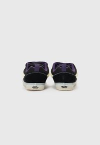 Baskets basses avec une tige en daim noir, des accents violets et des semelles blanches. Présentent des lacets contrastants et un logo sur le talon.