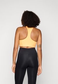 Sostenedor deportivo naranja con diseño de espalda nadador, tejido suave y acentos cosidos, combinado con leggings negros de cintura alta.