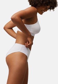 Bralette blanco de algodón y braguitas de talle alto con una textura suave y diseño sin costuras, mostrados de perfil contra un fondo liso.