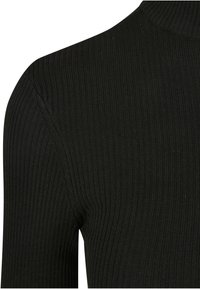 Primo piano di tessuto a maglia a coste nero che mostra la spalla e la zona superiore della manica di un capo aderente.
