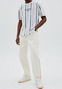 Camiseta de manga corta a rayas en blanco, azul y rosa; impresión del logotipo en el pecho. Pantalones rectos blancos, zapatillas blancas con suela de goma.