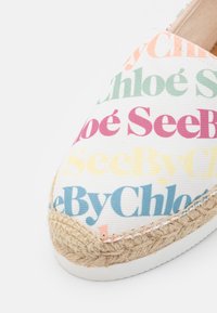Botte plate espadrille avec un motif de texte multicolore "See By Chloé" sur une tige en tissu blanc et des détails en jute tressé sur la semelle.