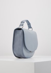 Sac en cuir bleu clair avec une bandoulière détachable, devant lisse et côté en daim. Il dispose d'un rabat arrondi et de quincaillerie en argent.
