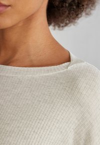 Světle šedý žebrovaný top s širokým, kulatým výstřihem a měkkou, texturovanou tkaninou, která vykazuje jemné vertikální pruhy.