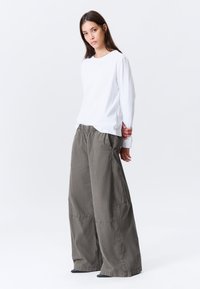 Chemise blanche à manches longues et pantalon gris à jambes larges avec une taille élastique, présentant une coupe décontractée et des détails de couture visibles.