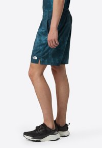 Sport shorts in dark teal with a tie-dye pattern, featuring an elastic waistband and side slits. Pairing with black running shoes.