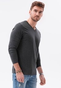 Långärmad kolgrå t-shirt med v-ringning, mjukt tyg, figursydd design. Bärs med ljusblå slitna jeans och ett accessoararmband. Vit bakgrund.