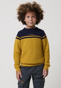 Rumeno in mornarsko moder stricken pulover s teksturiranim tkanim vzorcem in rebrastimi manšetami. Vsebuje logotip "KOROSHI BRAND" v rumeni barvi.