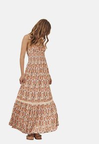 Vestido maxi con cuerpo fruncido, tirantes finos y falda en capas. Presenta un elaborado patrón floral en colores cálidos sobre un fondo claro.
