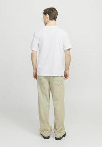 Witte t-shirt met korte mouwen en ronde hals, gecombineerd met lichtbeige, loszittende broek met achterzakken en subtiele stiksels.