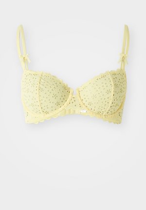 Soutien-gorge en dentelle jaune avec des bords festonnés et des motifs floraux découpés. Dispose de bretelles réglables et de petits nœuds sur les deux bretelles.