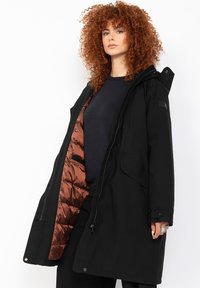 Sort parka med hætte, udstyret med en blank brun quiltet inderside, lynlås lukning og sidelommer. Lavet af et vejrbestandigt materiale.
