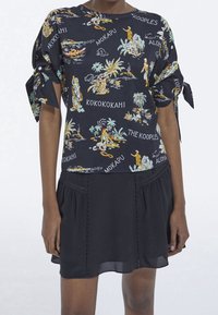 Top nero a fantasia con disegni tropicali e maniche corte a sbuffo, abbinato a una gonna nera con orlo arricciato e cuciture decorative.