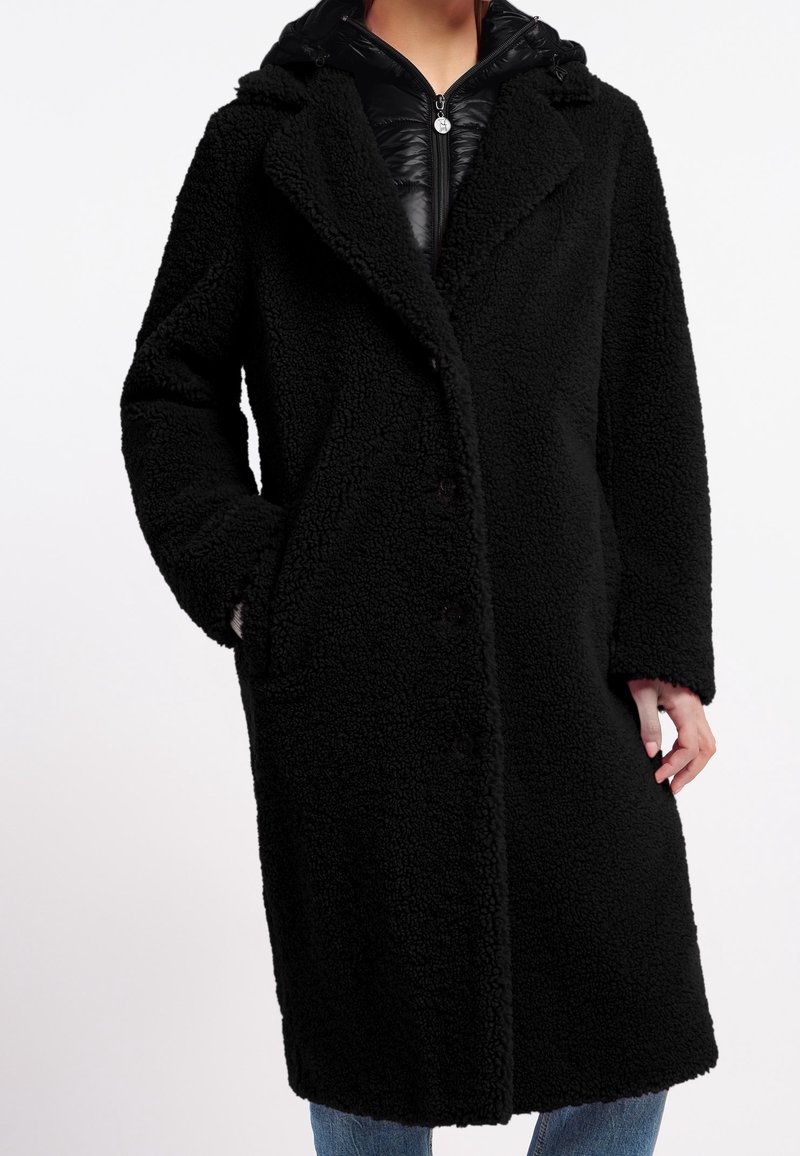 Zwarte faux fur jas met een relaxte pasvorm, voorzien van brede revers, knopen aan de voorkant en zijzakken. Kap met een binnenlaag in zwart glanzend materiaal.