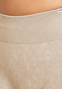 Fascia in maglia beige e morbido tessuto dei pantaloni a vita alta, che mostra parte della schiena inferiore di una persona.