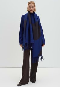 Sciarpa lavorata a maglia blu e nera con bordi frangiati, caratterizzata da audaci forme geometriche. Il tessuto appare morbido e caldo, adatto per il clima più freddo.