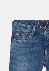 Vaqueros de mezclilla azul oscura con una cinturilla cosida, bolsillos delanteros y un pequeño acento a rayas rojas y blancas en el bolsillo izquierdo.