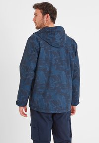 Navy blue waterproof jacket featuring a textured abstract pattern, adjustable hood, and elastic cuffs, worn over dark pants.